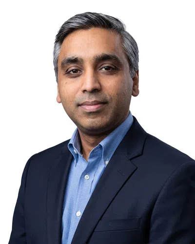 Professional portrait of a confident middle-aged man with gray hair wearing a blue shirt and dark blazer