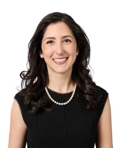 Smiling woman with short curly dark hair wearing a purple beaded necklace against a white background