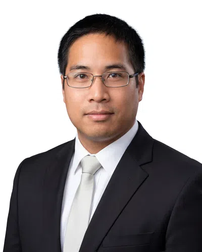 Professional man wearing glasses, black suit, white shirt, and silver tie against a white background