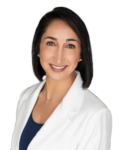Professional woman with dark hair smiling, wearing a white blazer and navy top against a white background