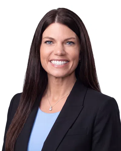 Smiling professional woman with long brown hair wearing a black blazer and blue top on white background
