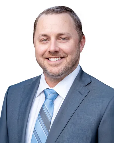 Smiling man with beard in blue suit and striped blue tie against white background