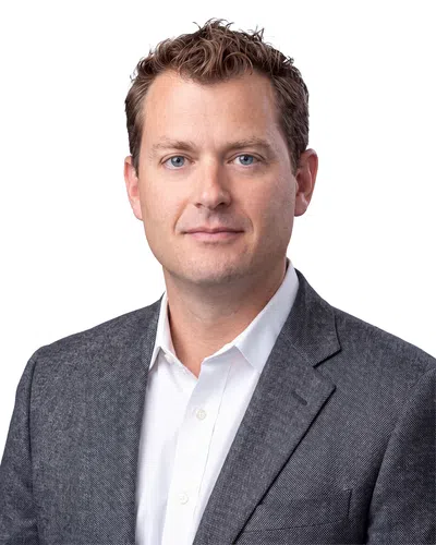 Professional headshot of a man with blue eyes wearing a white shirt and gray blazer on white background