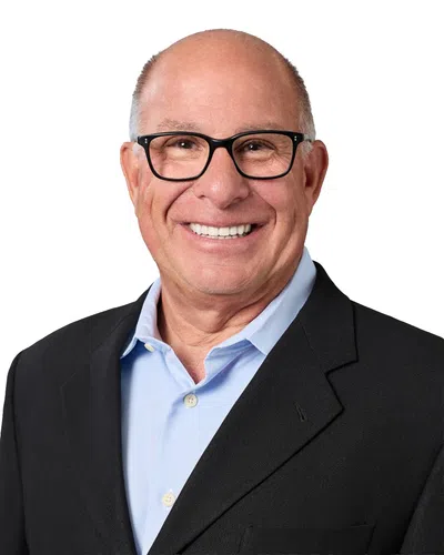 Smiling bald man wearing black glasses and a white shirt with a dark jacket against a white background