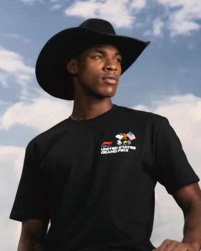 Young man wearing a black cowboy hat and a United States Grand Prix t-shirt under a cloudy sky.