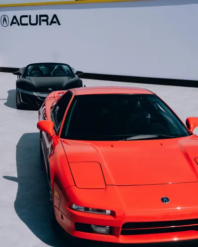 Red and black Acura sports cars parked outdoors in front of a white wall with Acura logo.