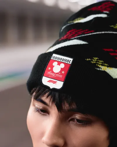Close-up of person wearing black beanie with Mickey Mouse and Formula 1 logo patch.