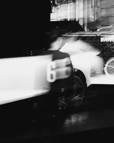 Black and white blurred motion image featuring a person with number 65 on their back in front of a vehicle.