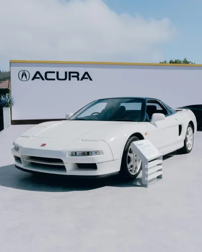 White Acura NSX sports car displayed outdoors with Acura logo and information plaque under blue sky.