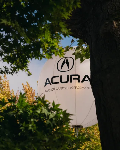 White Acura branded balloon with logo and tagline seen through green tree leaves on a sunny day