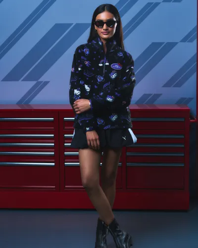 Woman wearing black patterned jacket, black skirt, sunglasses, and boots standing in front of red tool cabinets.