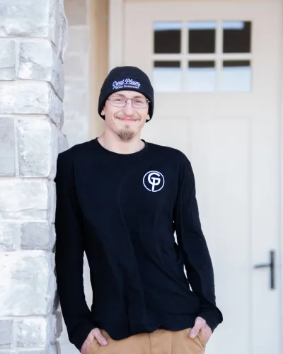A young man in a black long-sleeve shirt with a logo, standing casually against a stone wall.