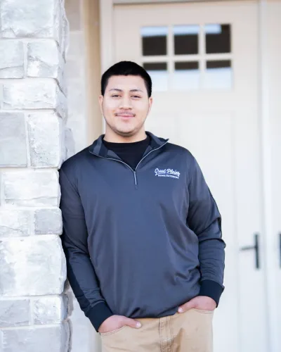 Man in a gray quarter-zip pullover stands against a stone wall, smiling confidently.