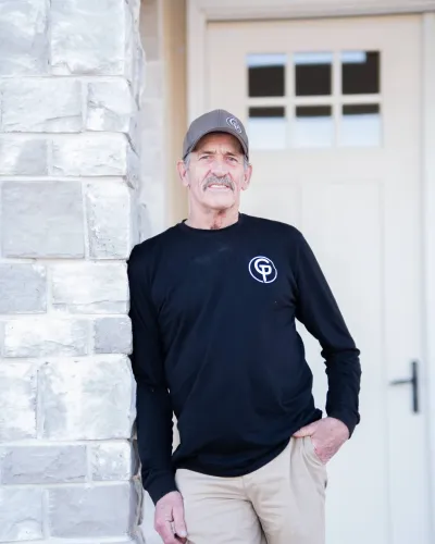 Man in a black long-sleeve shirt and shorts stands against a stone wall by a door.