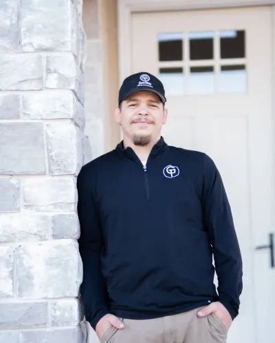 Man in a black long-sleeve shirt and cap stands against a stone wall by a door.
