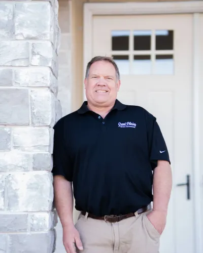 Smiling man in black shirt leaning against a stone column by a door.