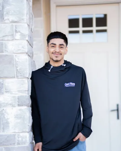 Smiling young man in a black sweatshirt poses by a stone column outside a building.