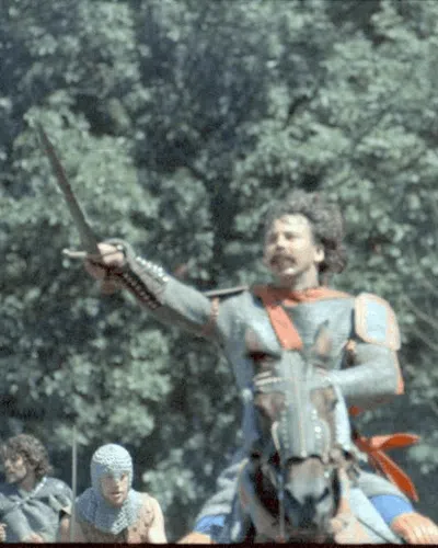 Medieval knight in armor raising sword on horseback with other armored men in forest setting.