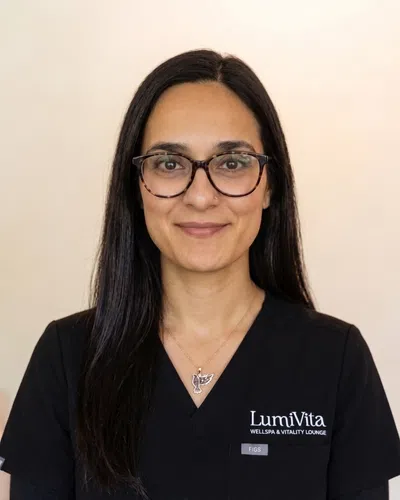 Woman with long dark hair and glasses wearing a black LumiVita WellSpa & Vitality Lounge uniform with a dove necklace.