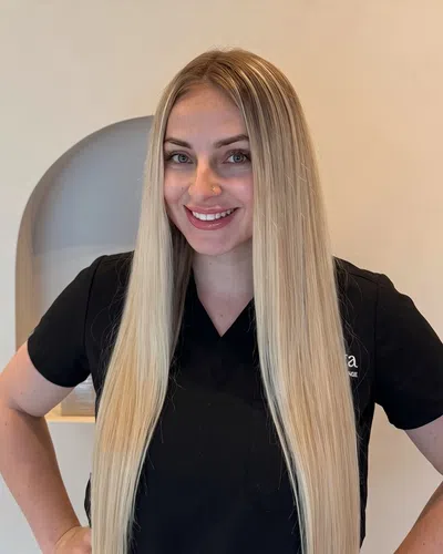 Smiling woman with long straight blonde hair wearing a black shirt against a neutral background