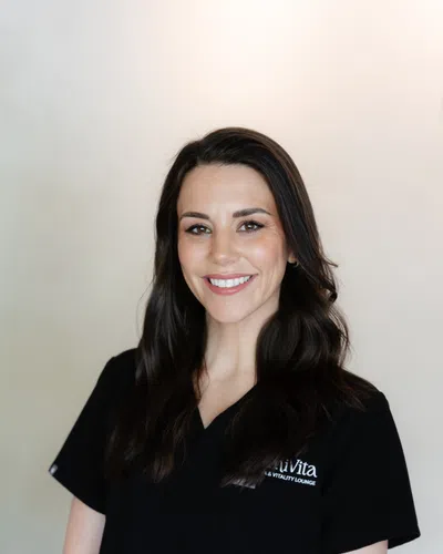 Smiling woman with dark hair wearing black medical scrubs standing against a neutral background
