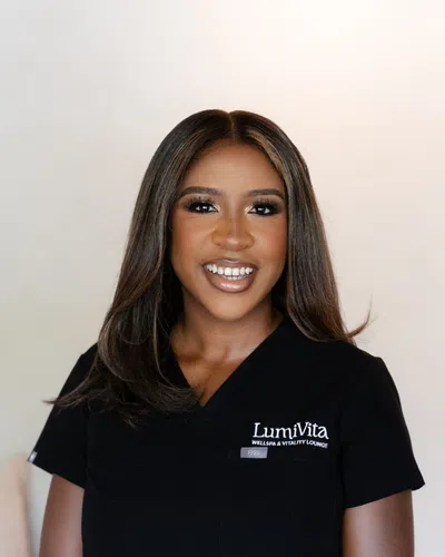 Smiling woman with straight shoulder-length hair wearing a black LumiVita spa uniform against a light background