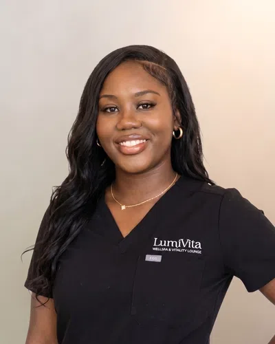 Smiling woman with long black hair wearing black LumiVita medical scrubs with logo and name tag.