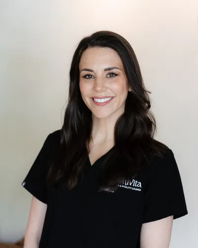 Smiling woman with dark hair wearing black medical scrubs standing against a neutral background