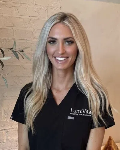Smiling woman in black scrubs seated in cozy wellness lounge with LumiVita sign and decorative pillows.