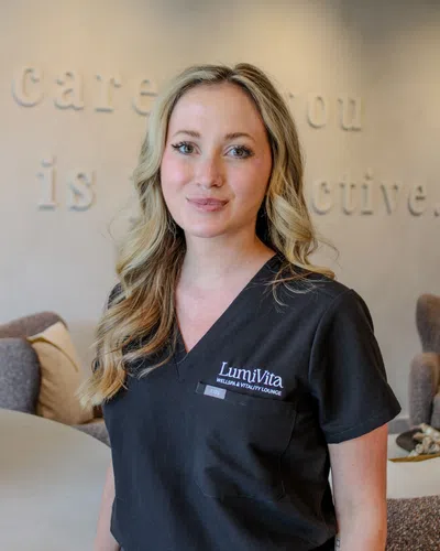 Smiling wellness professional in black LumiVita scrubs standing in a spa lounge with soft decor background
