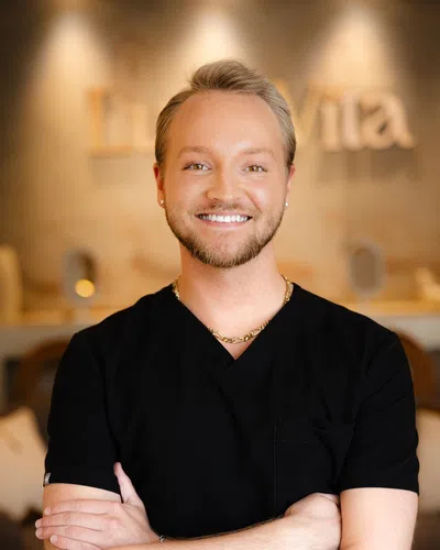 Smiling young male healthcare professional in black scrubs standing with arms crossed in a warm clinic setting