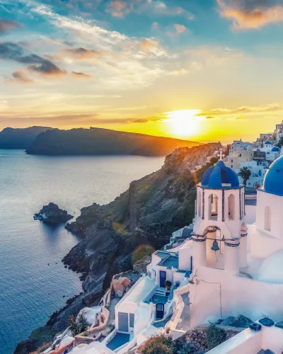 a white building on a cliff by the water with Santorini in the background