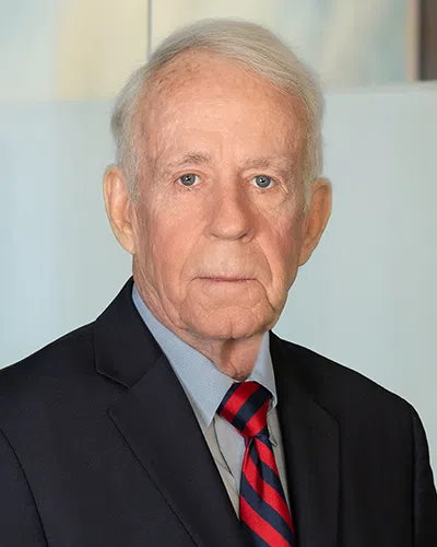Professional older man in suit with red and blue striped tie posing against light background.
