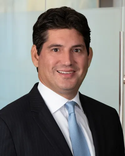 Smiling man in dark suit and white shirt posing against plain gray background