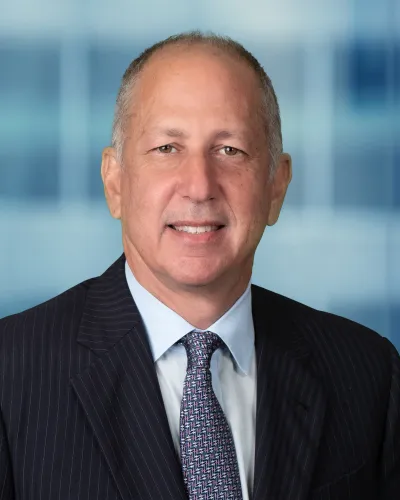 Mature man in pinstripe suit and patterned tie smiling against a blurred blue office background.
