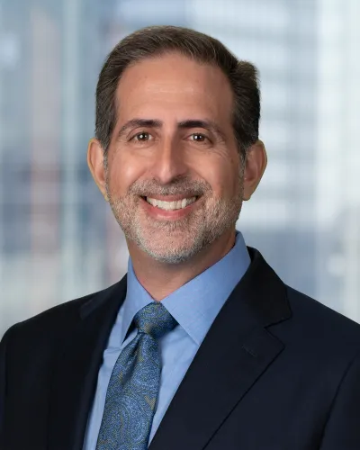 Middle-aged man with short dark hair and beard wearing a light purple dress shirt smiling against gray background
