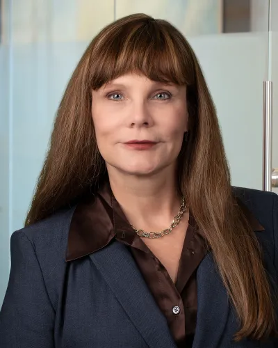 Professional headshot of a woman with long brown hair, wearing a black top against a neutral backdrop.