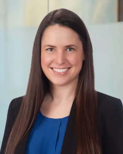 Smiling woman with long brown hair wearing a blue top and black and white patterned cardigan.
