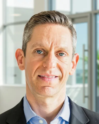 Professional middle-aged man with blue eyes wearing a suit and light blue shirt in a modern office setting