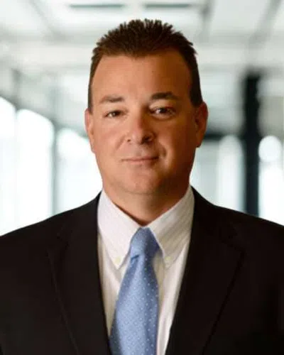 Professional man in business suit and blue tie standing in a modern office with blurred windows behind him