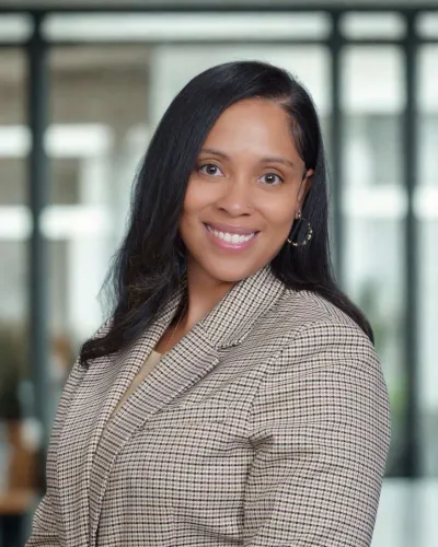 Smiling woman with long black hair wearing a checkered blazer in a modern office setting