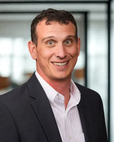 Smiling man in business attire with dark blazer and striped white shirt in office setting