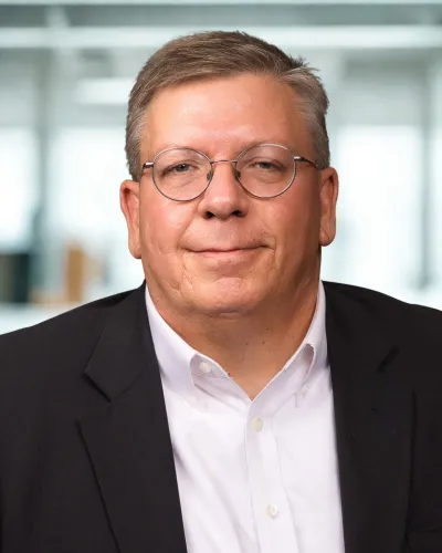 Middle-aged man with glasses wearing a black blazer and white shirt in a modern office setting