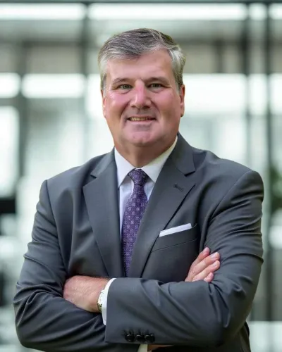 Smiling middle-aged man in gray suit and purple tie with arms crossed in modern office setting