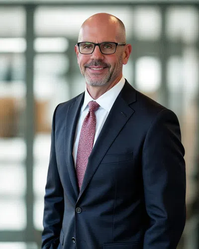 Professional middle-aged man in glasses wearing a dark suit and red tie, smiling in a modern office setting