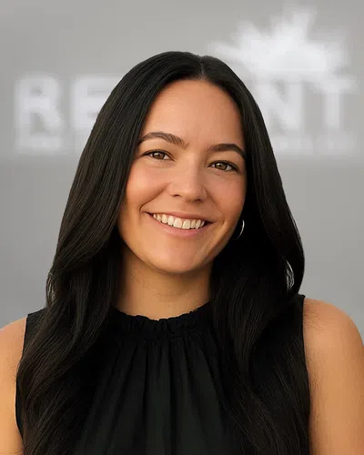 Smiling woman with long black hair wearing a black sleeveless top against a grey blurred background.