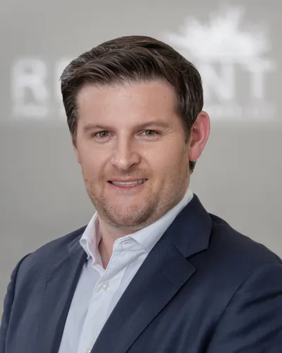 Professional man in navy suit and white shirt smiling against blurred neutral background.