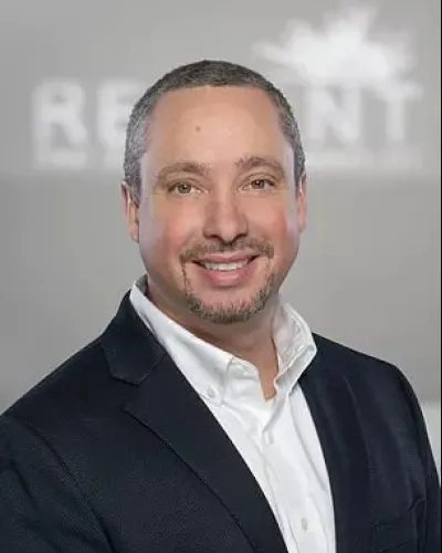 Smiling man in black suit jacket and white shirt with blurred logo background in professional headshot
