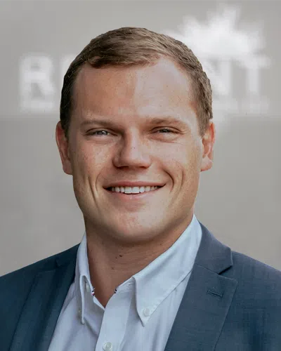 Smiling young professional man in a blue suit jacket and white shirt with blurred background.