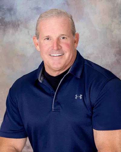 Smiling middle-aged man wearing a navy blue Under Armour polo shirt against a neutral backdrop